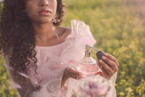 A person in a soft pink dress holds an elegant vintage perfume bottle, surrounded by lush greenery and a dreamy atmosphere.