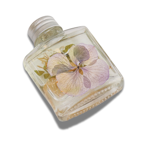 A glass bottle with a silver cap featuring a delicate pressed purple flower and green leaves inside.